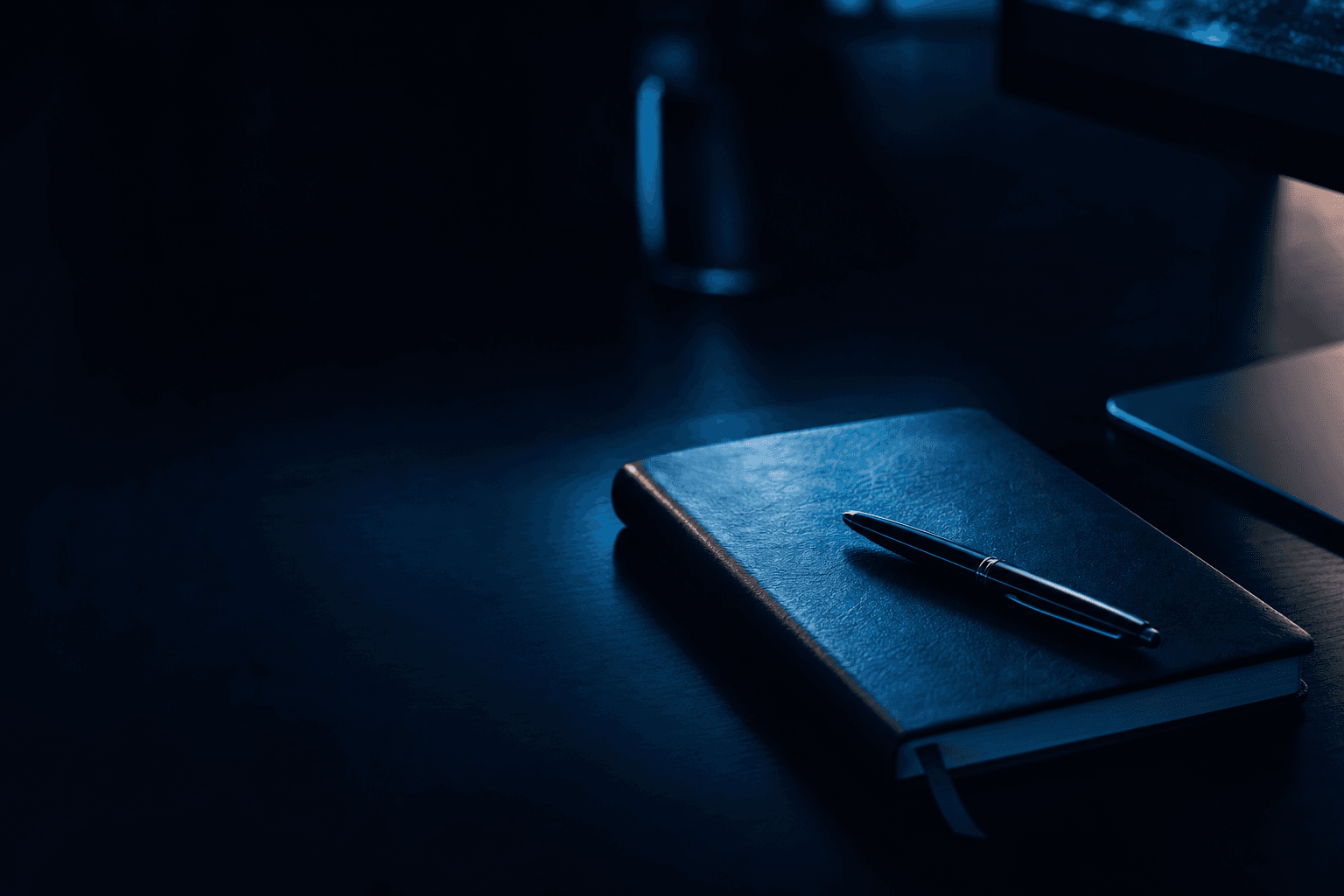 Closed leather notebook on a dark desk with a soft monitor glow at the frame's edge, signalling considered late-night SEO analysis